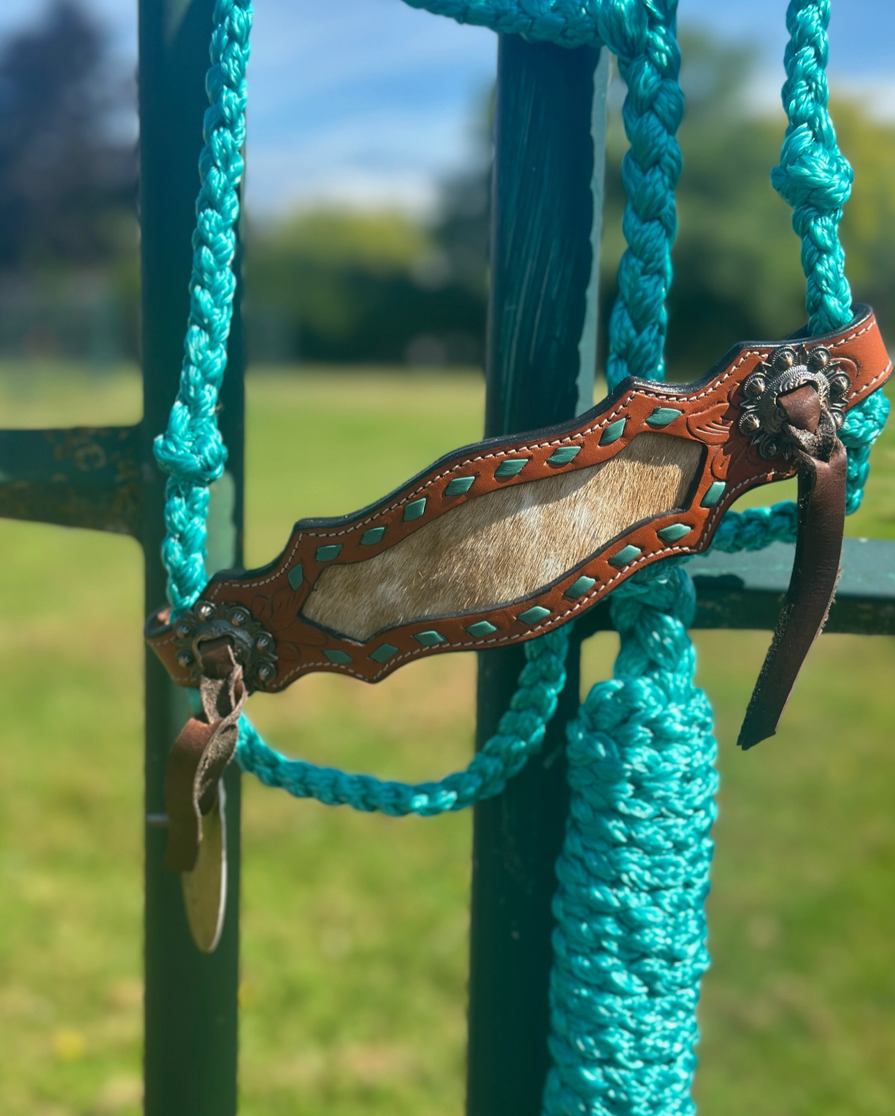 Decorative leather strap with metal buckle on a turquoise rope against a blurred green background
