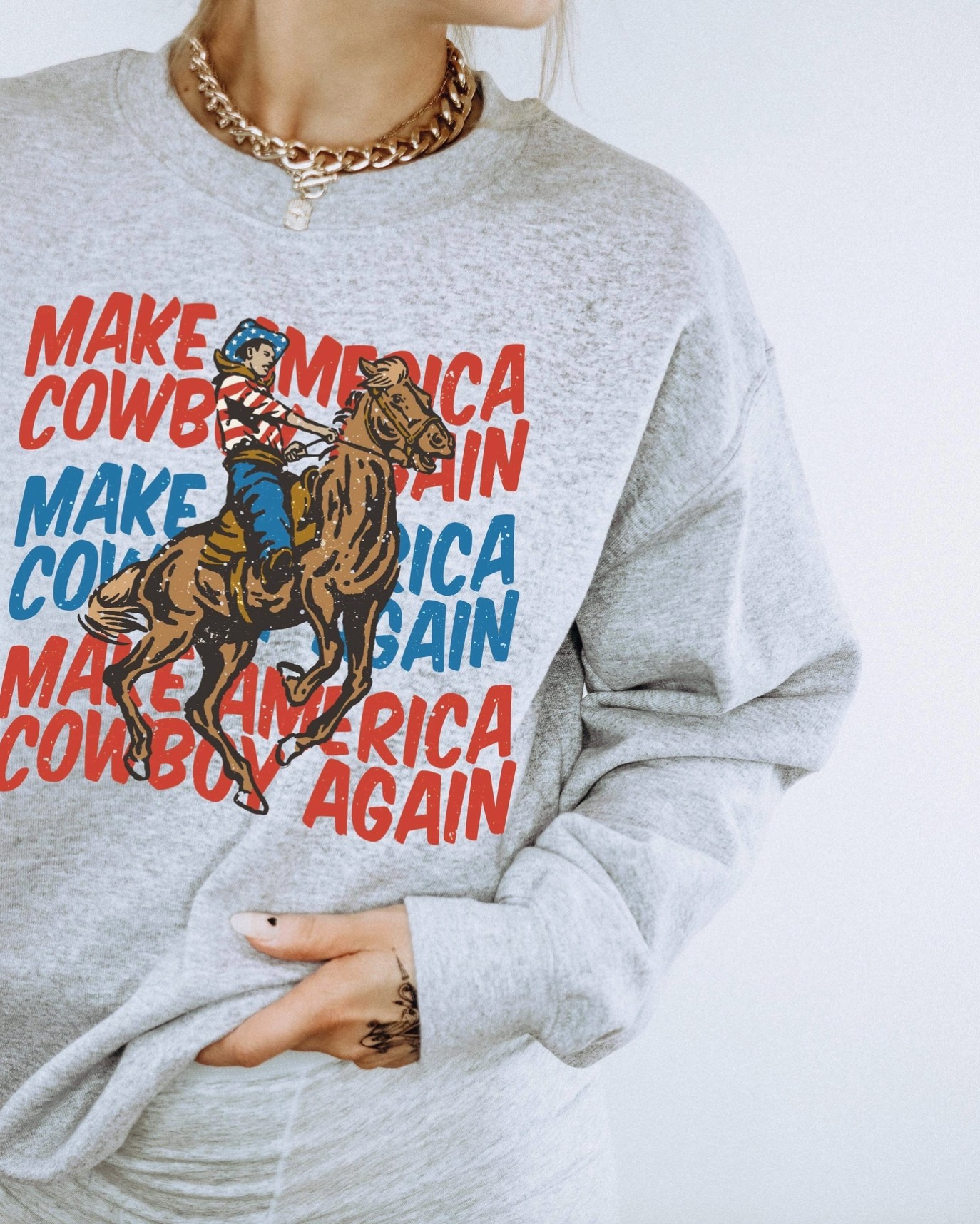 Gray sweatshirt with a graphic of a cowboy on a horse and text 'Make Cowboy America Again' on a white background.