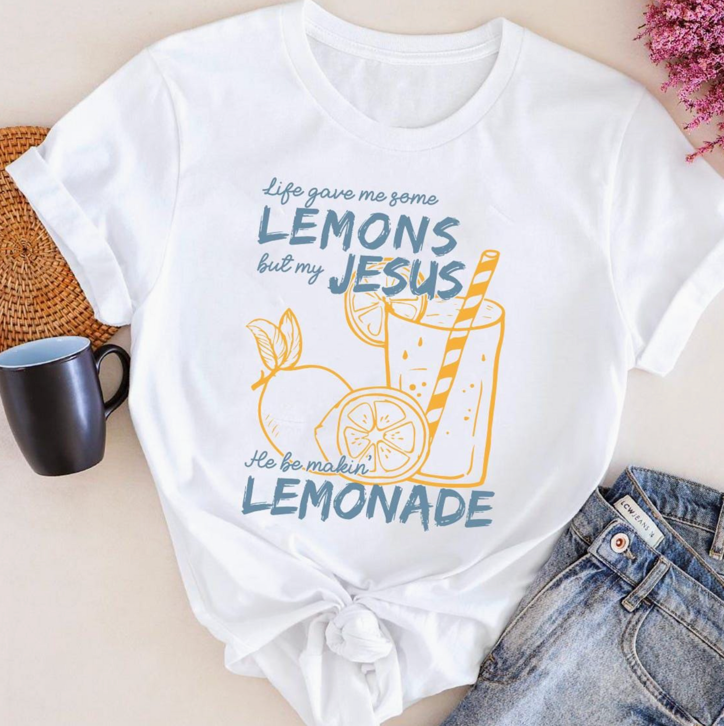 White t-shirt with lemonade graphic and text on a light surface with a mug and jeans.